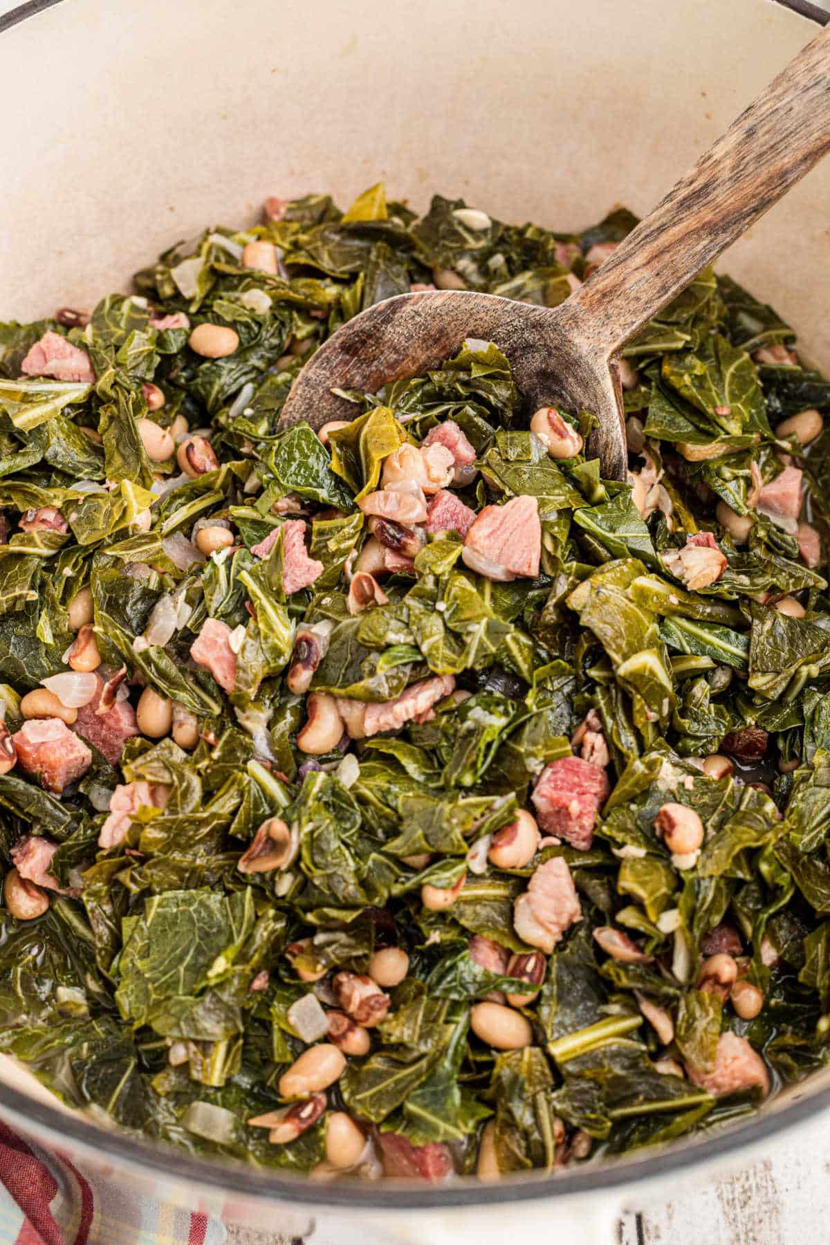 Closeup inside a pot with a spoon digging into the collard greens and black eyed peas.