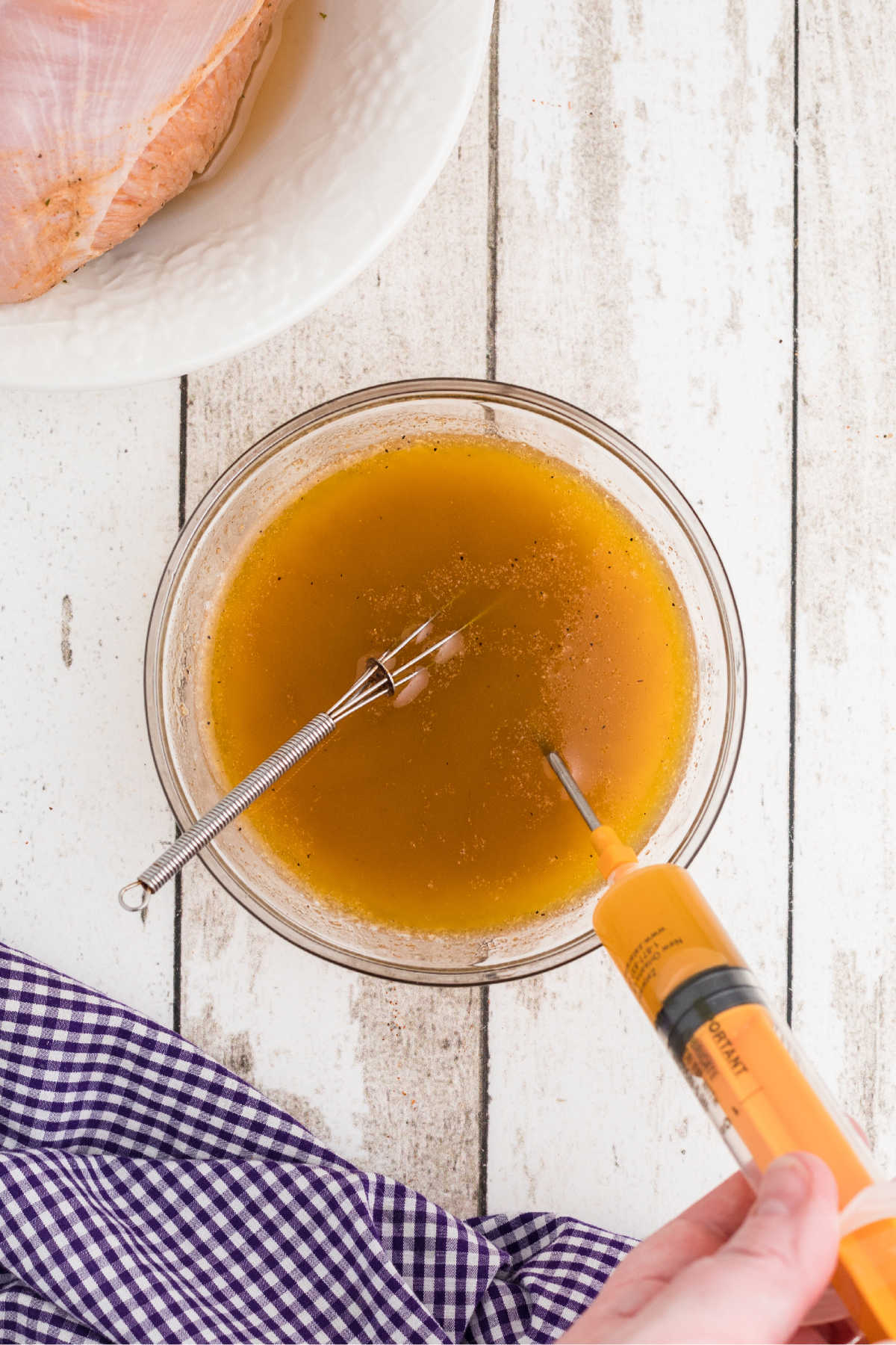A bowl full of seasonings and marinade, with a syringe filling up.