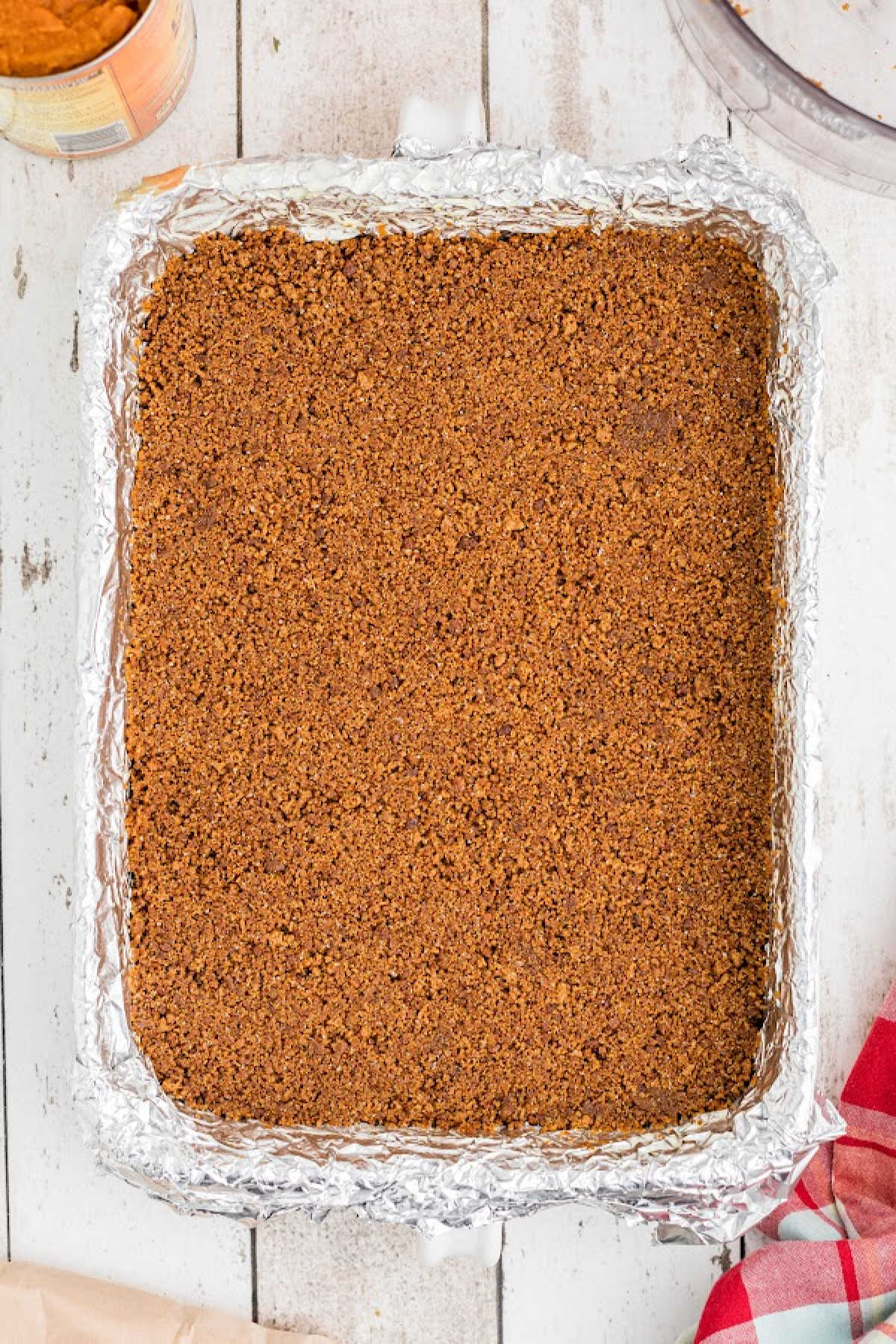 A large baking dish lined with foil and cookie crumb mixture pressed into it.