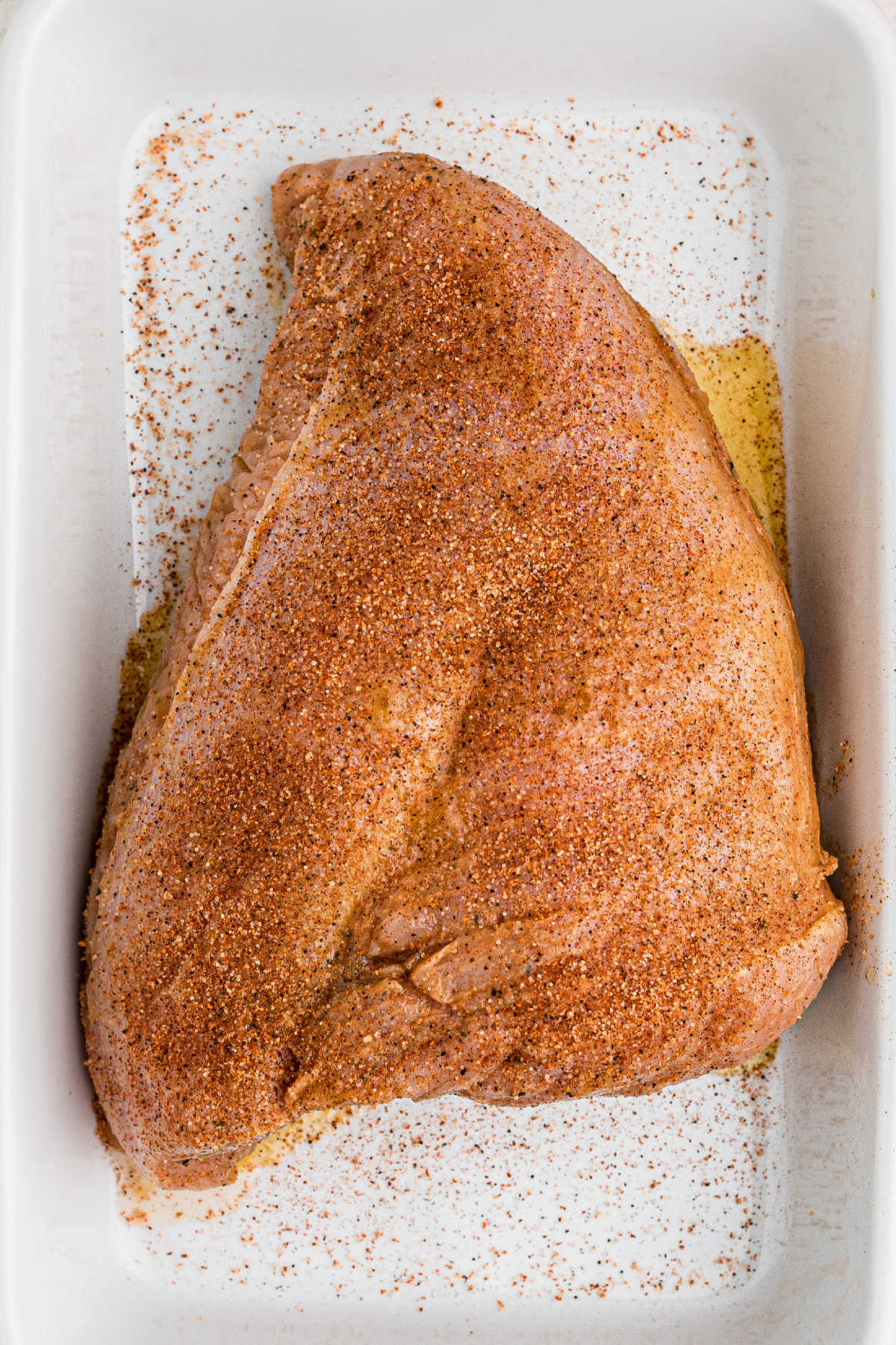 A turkey breast sitting in a dish full of seasoning.
