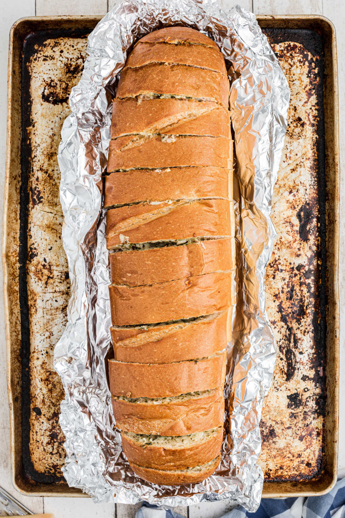 A baking sheet with a loaf of stuffed garlic bread still in foil.