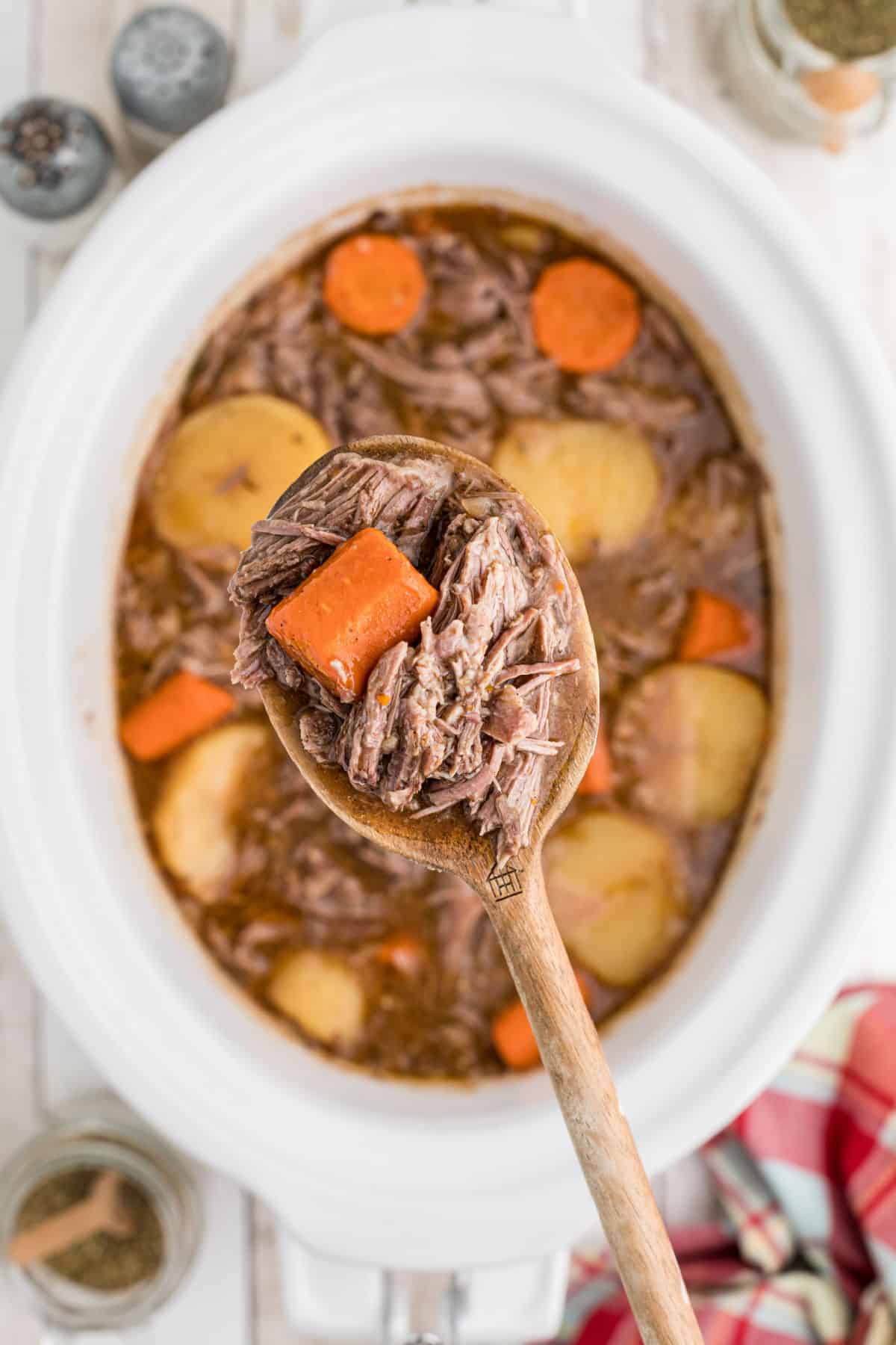 A spoon full of tri tip roast hovering above a slow cooker.