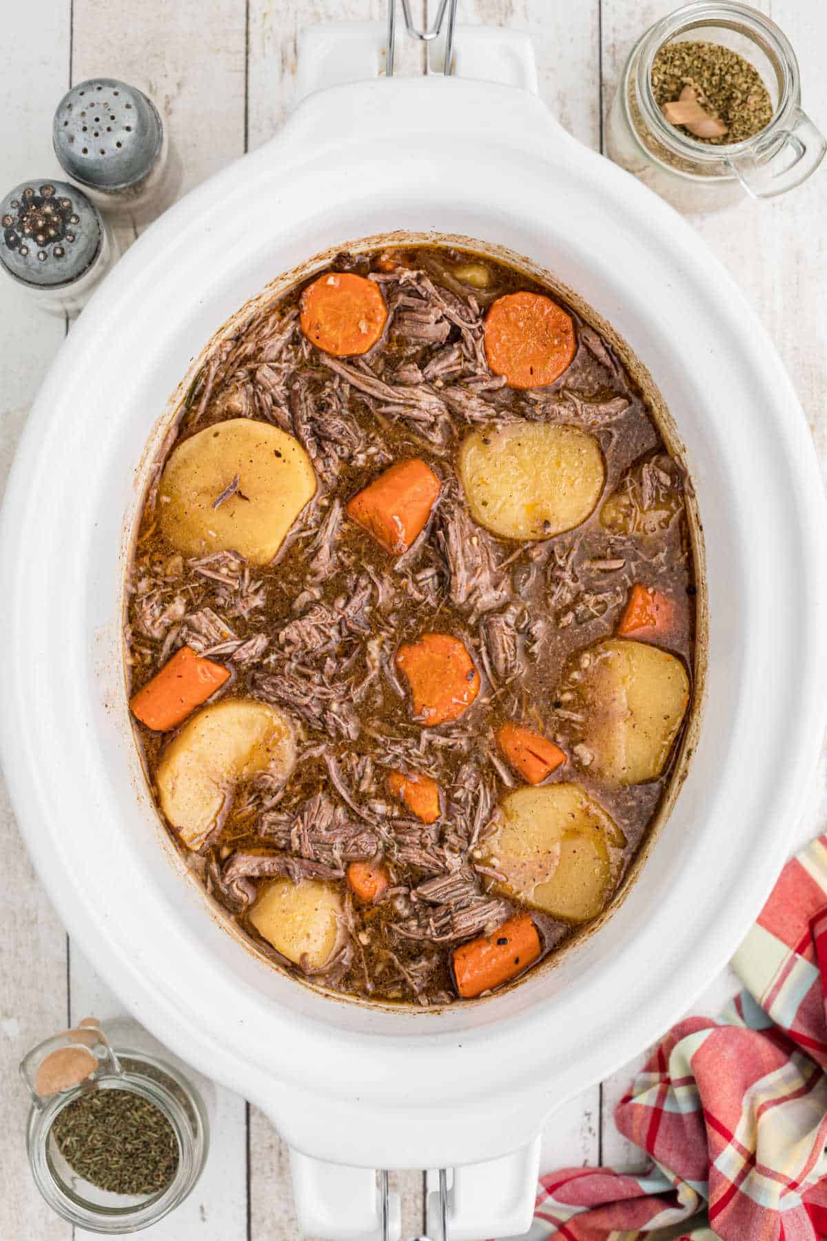 A white crock pot full of tri tip roast with carrots and potatoes.