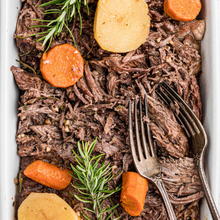 A close up of tri tip roast with potatoes and carrots and a pair of forks sitting in the dish.