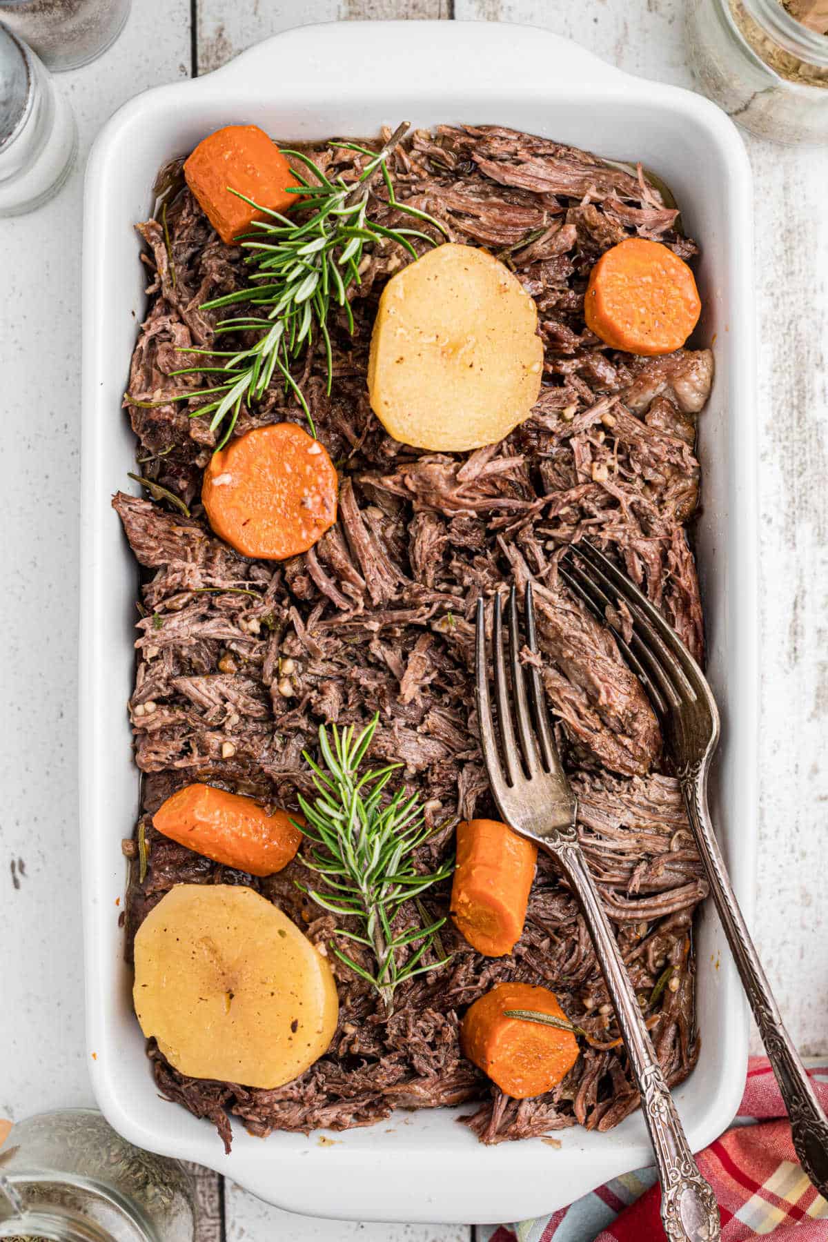 Overhead shot of a tri tip roast in a dish with potatoes and carrots and a pair of forks.