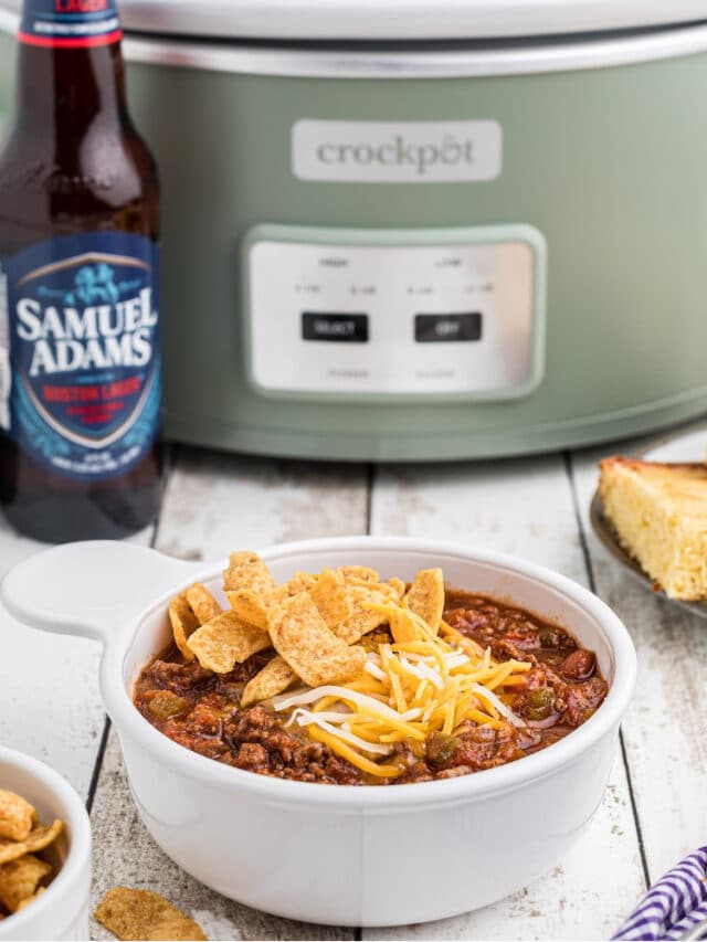 A bowl of beer chili sitting in front of a crock pot with a bottle of beer next to it.