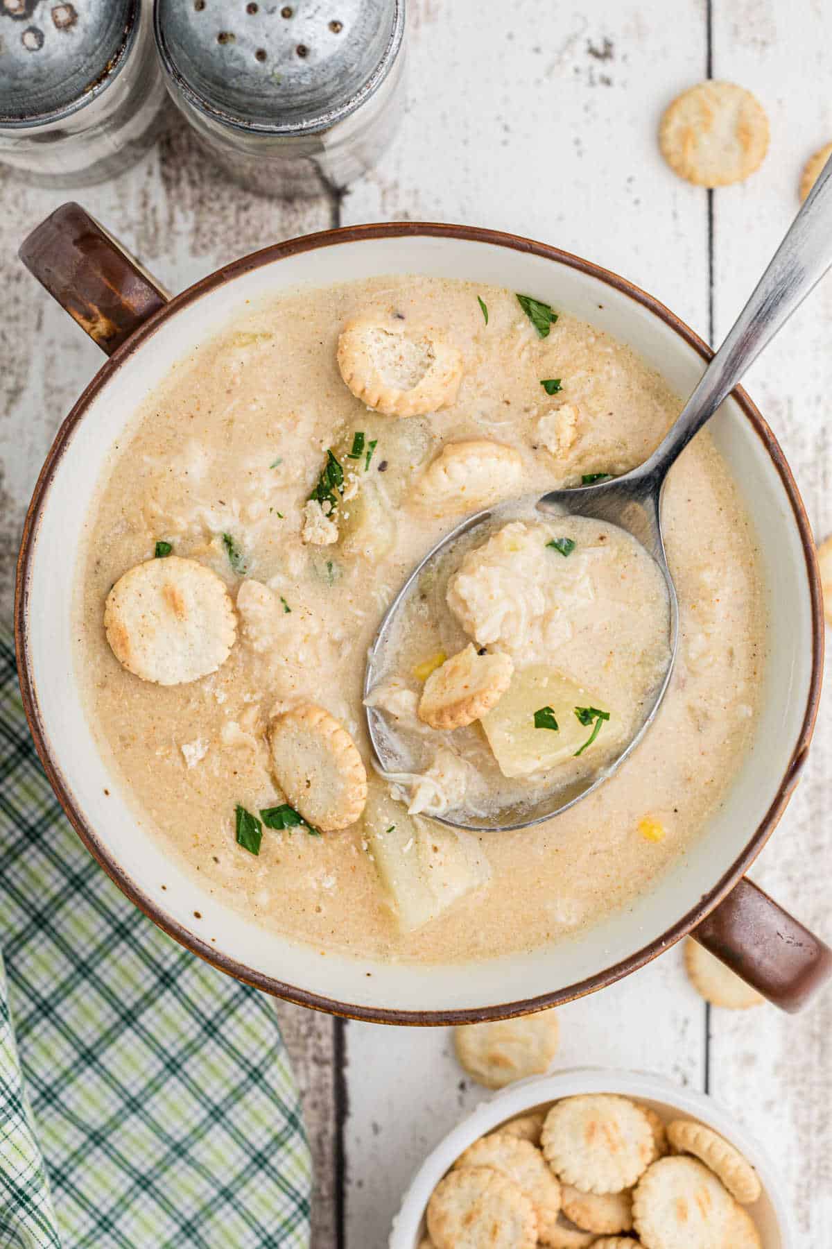 A portrait image of a bowl of crab chowder with a spoon digging into it.
