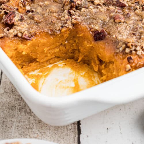 Close up of a corner of a dish of sweet potato casserole with a scoop missing.