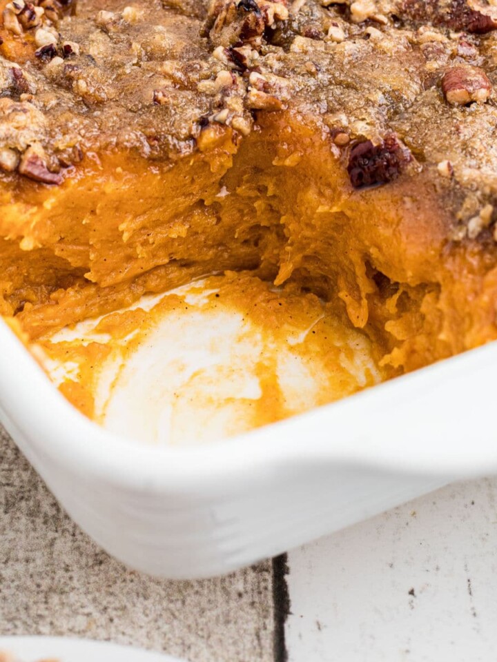 Close up of a corner of a dish of sweet potato casserole with a scoop missing.