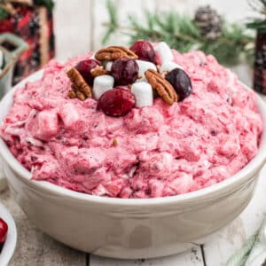 A cropped square image of a bowl of cranberry salad with some cranberries and marshmallows on top.