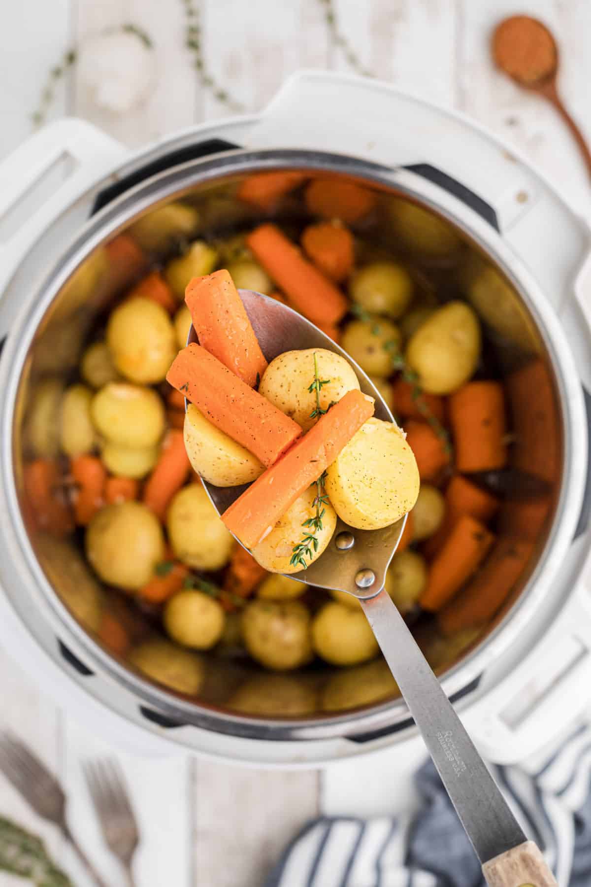Overhead shot of an instant pot with potatoes and carrots with a spoon overhead dishing out.