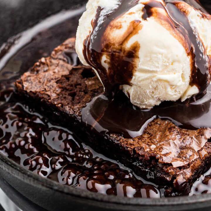Close up of a sizzling brownie in a pan with a scoop of ice cream and chocolate sauce on top.
