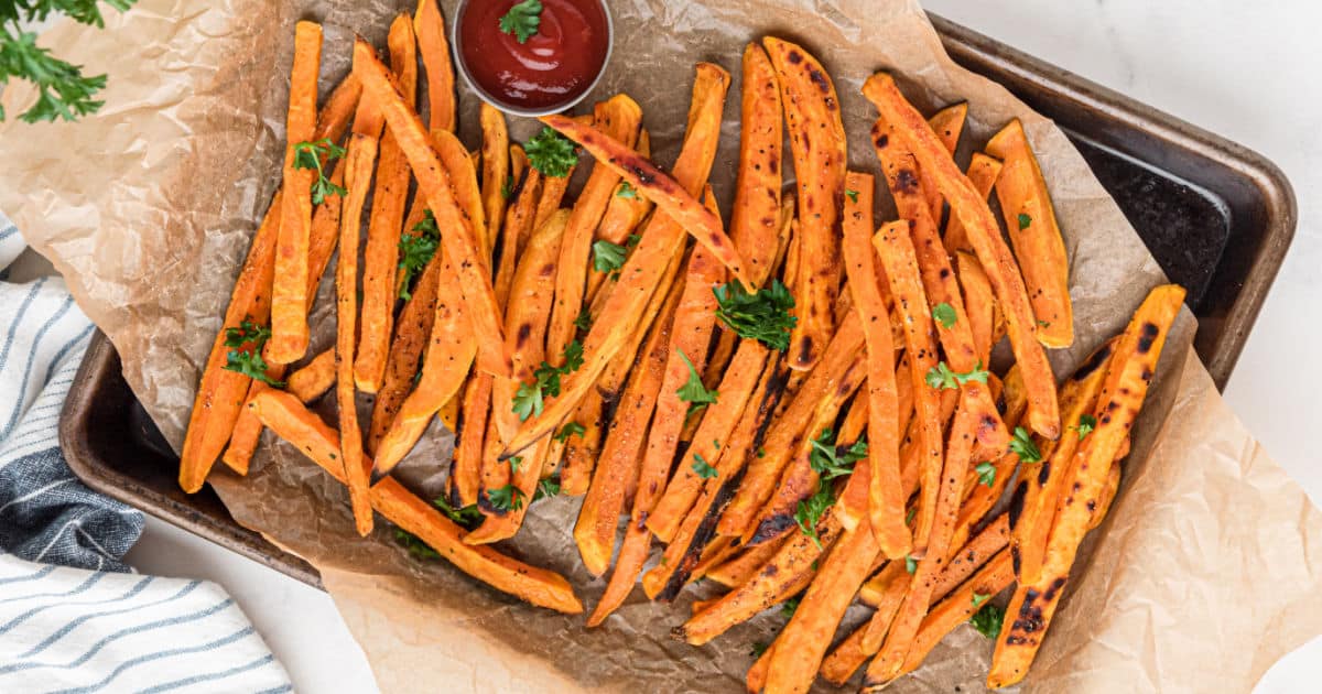 A tray full of crispy sweet potatoes, next to some dip.