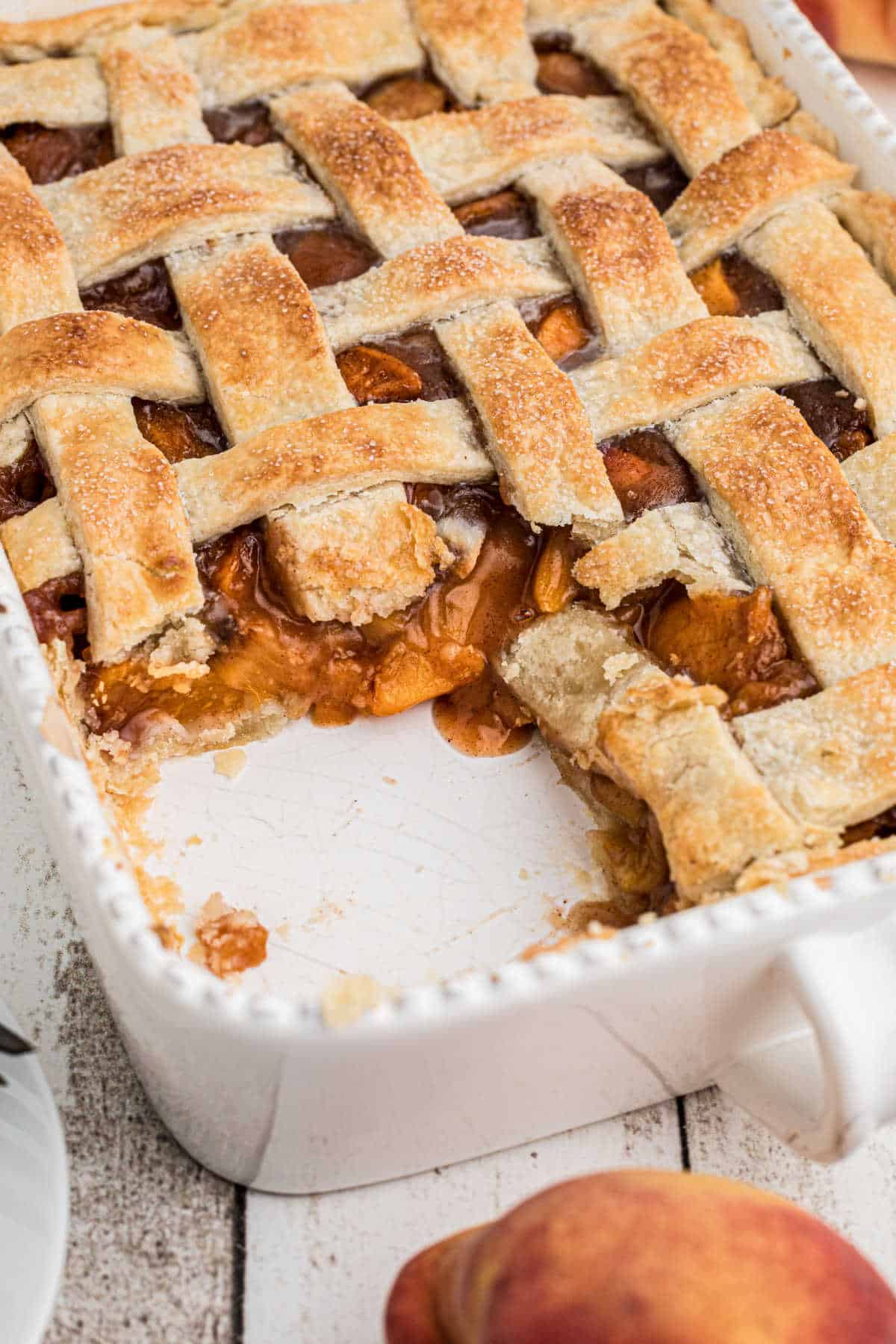 Hero image of a dish with a southern peach cobbler recipe with pie crust, and a scoop missing.