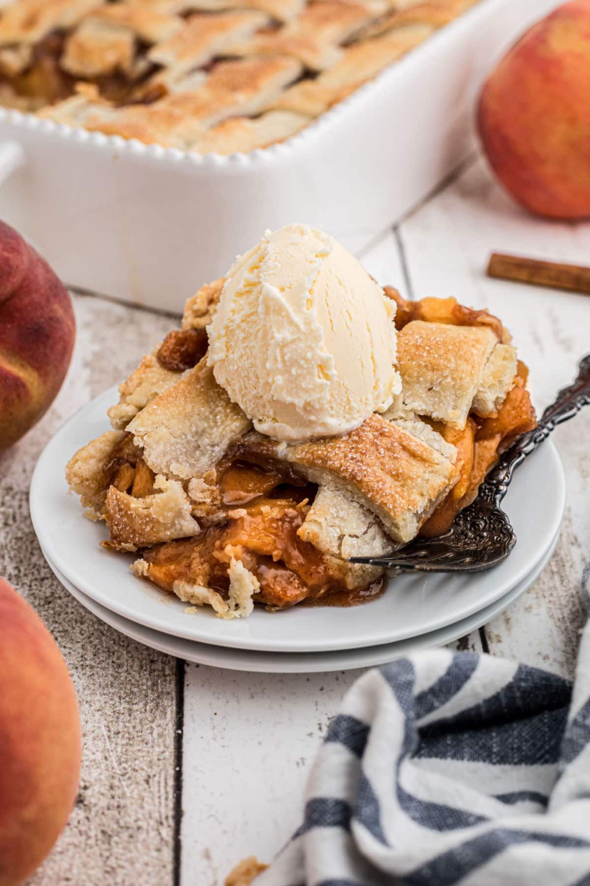 Dished out plate of southern peach cobbler with pie crust, and a scoop of ice cream on top.