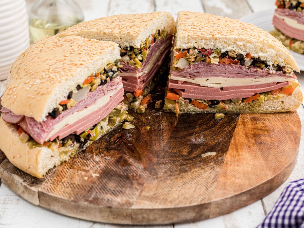 Landscape image of a Cajun Muffuletta Sandwich cut into four, with one slice missing.