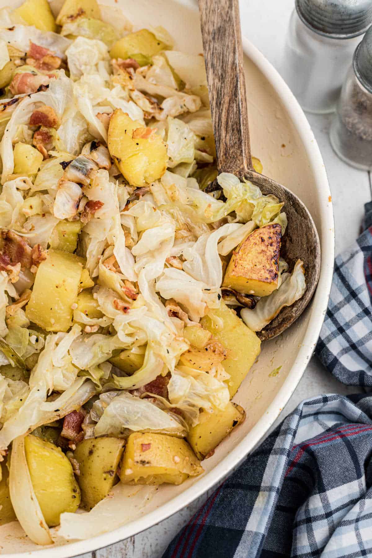Close up side shot of a skillet of fried cabbage and potatoes with a spoon digging in.