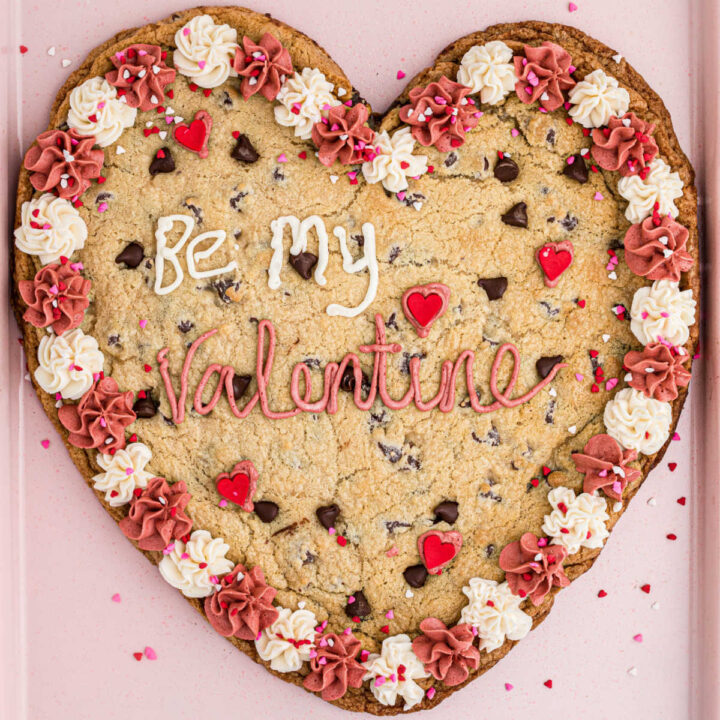A giant valentines cookie on a pink baking sheet.