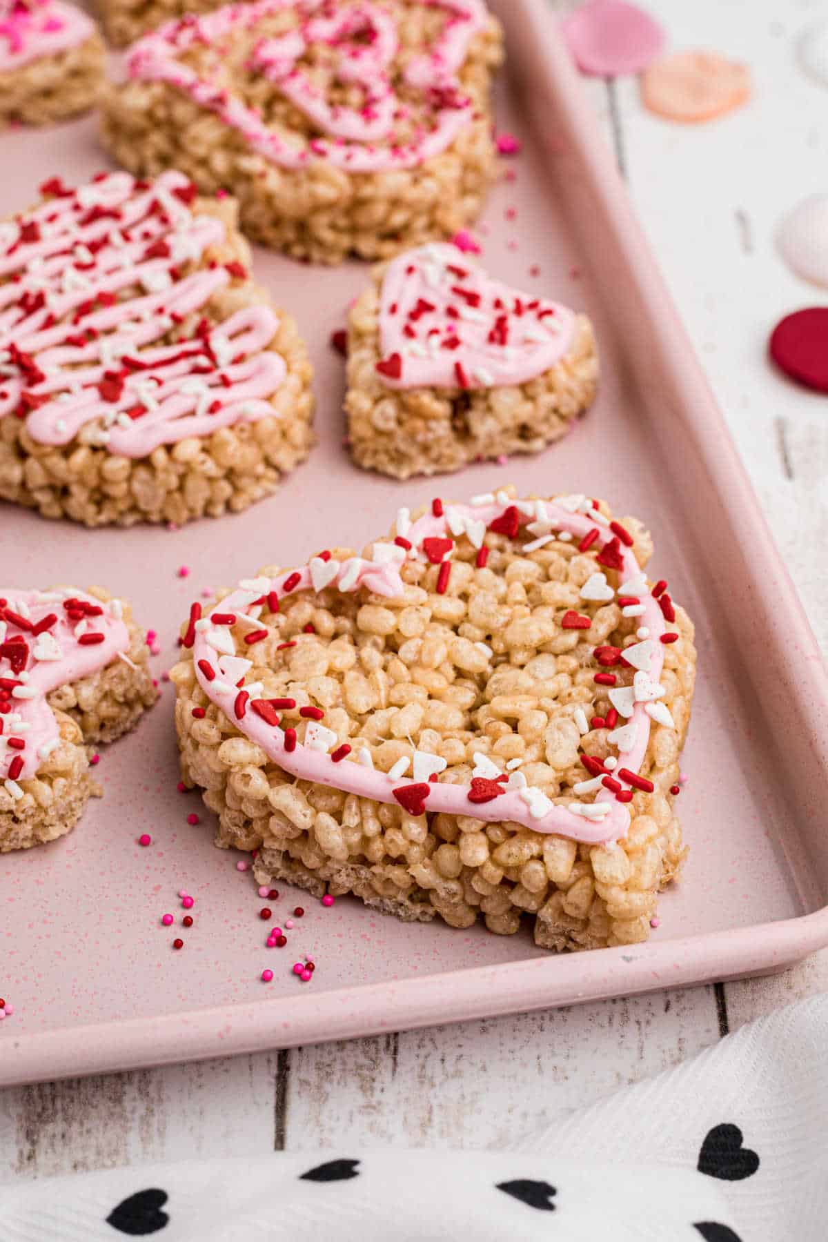Side shot of a tray full of heart shaped rice krispie treats, with frosting and sprinkles.