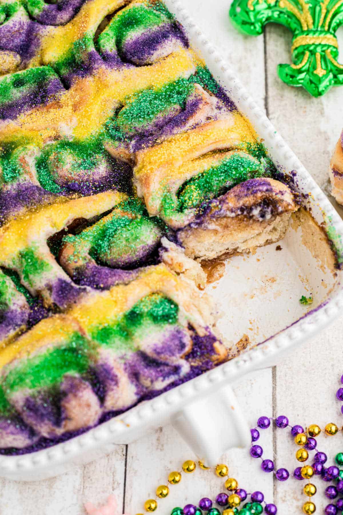 Angled shot of a pan full of king cake cinnamon rolls with one taken.