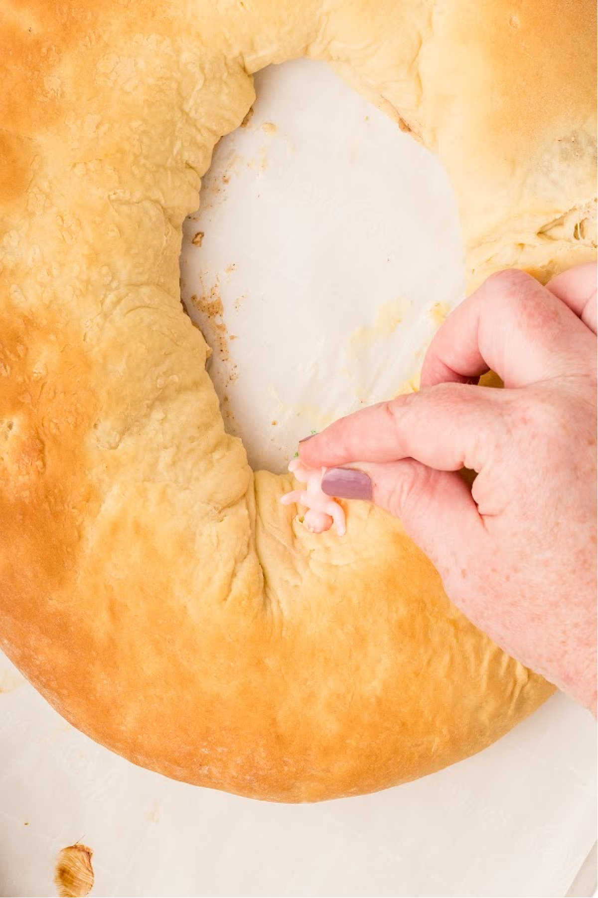 A plastic king cake baby being pushed into the king cake.