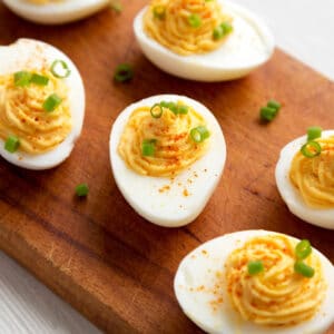 A wooden board with some deviled eggs sprinkled with green onions.