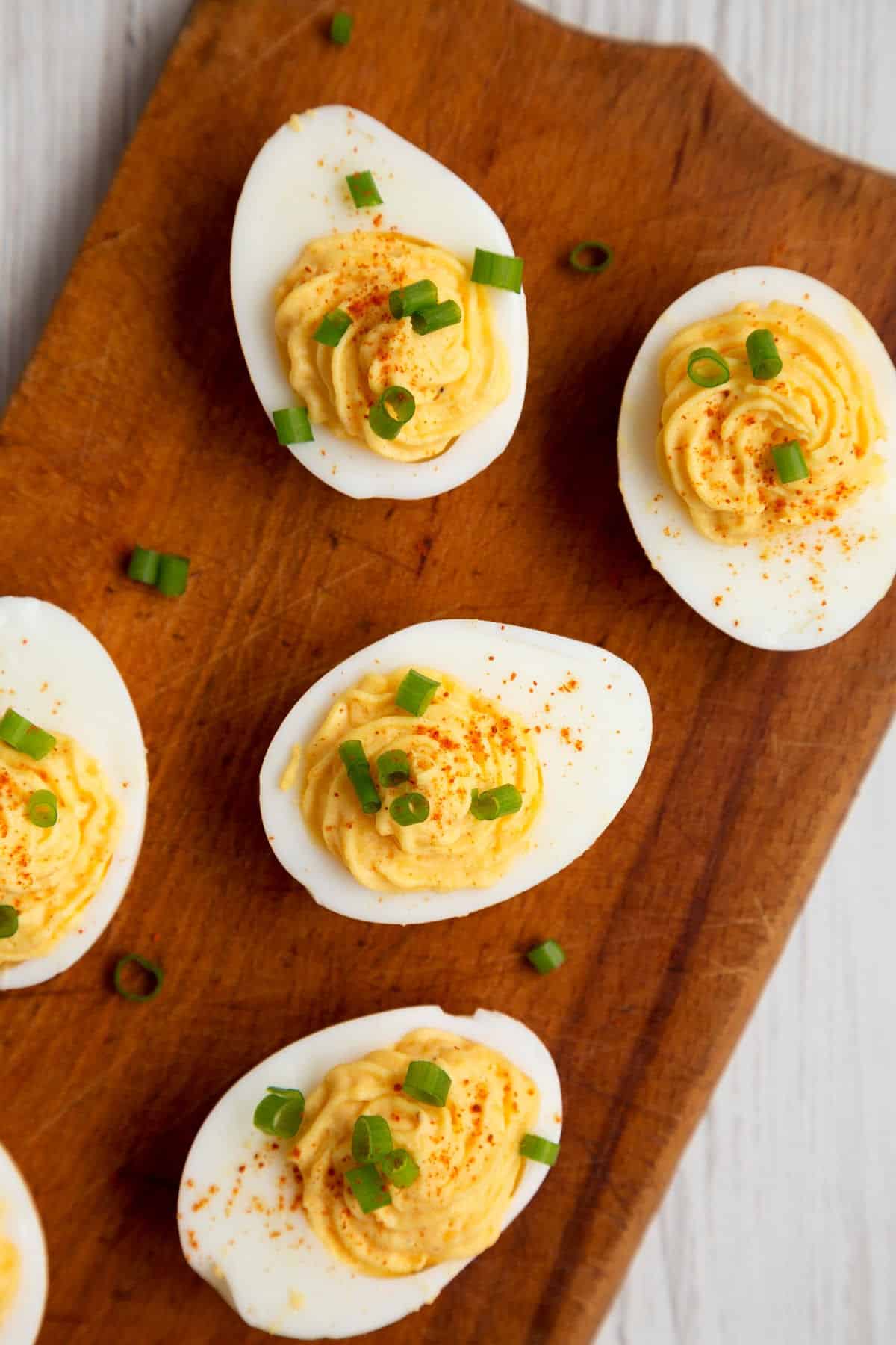 A wooden board with deviled eggs, sprinkled with green onions.