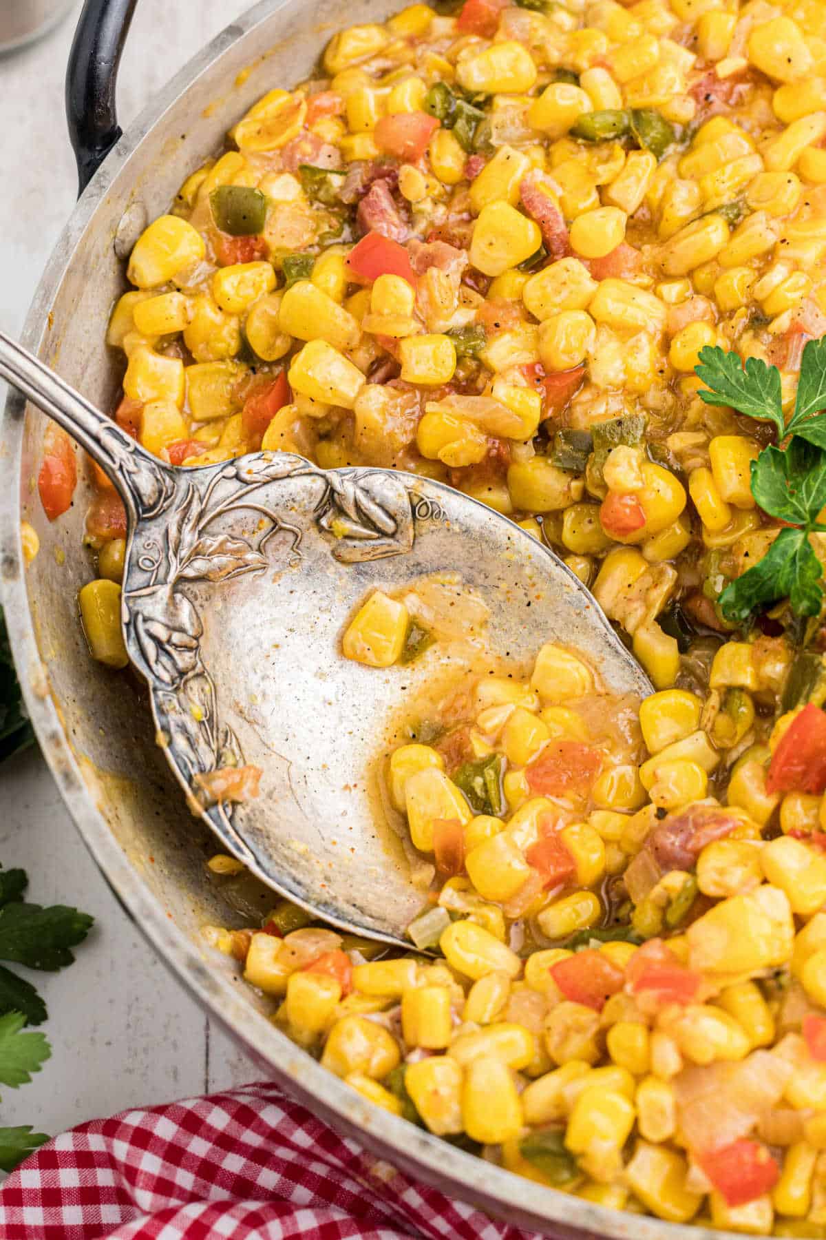 Close up side angle shot of a skillet with cajun corn maque choux and a spoon digging in.