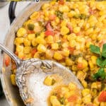 A long image of a close up skillet with cajun corn maque choux, with text overlay for pinterest.
