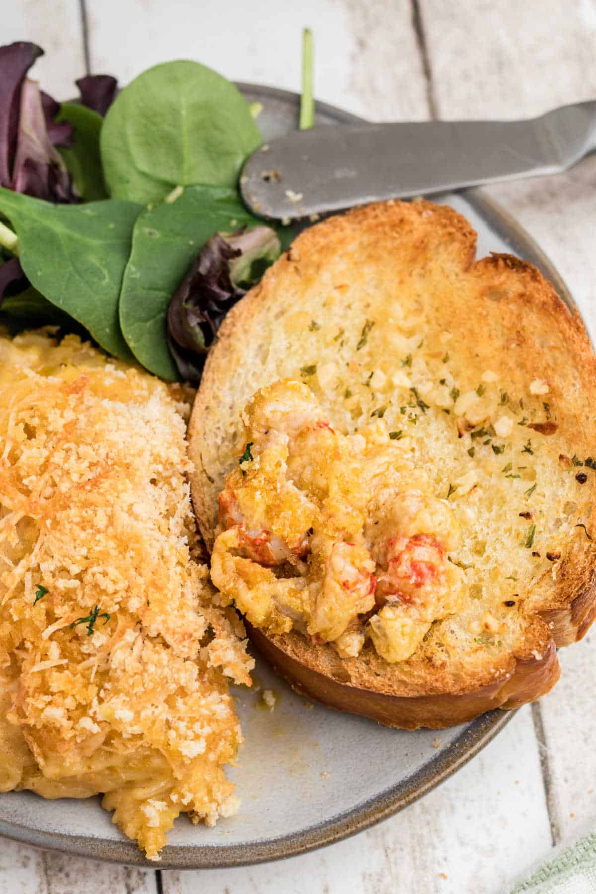 Close up of a piece of garlic toast with some crawfish au gratin.