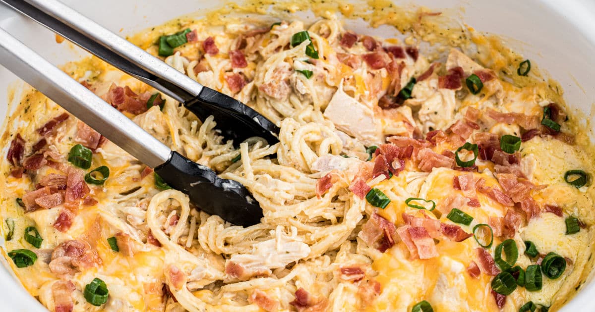 Close up of crock pot ranch chicken spaghetti being picked up with tongs.
