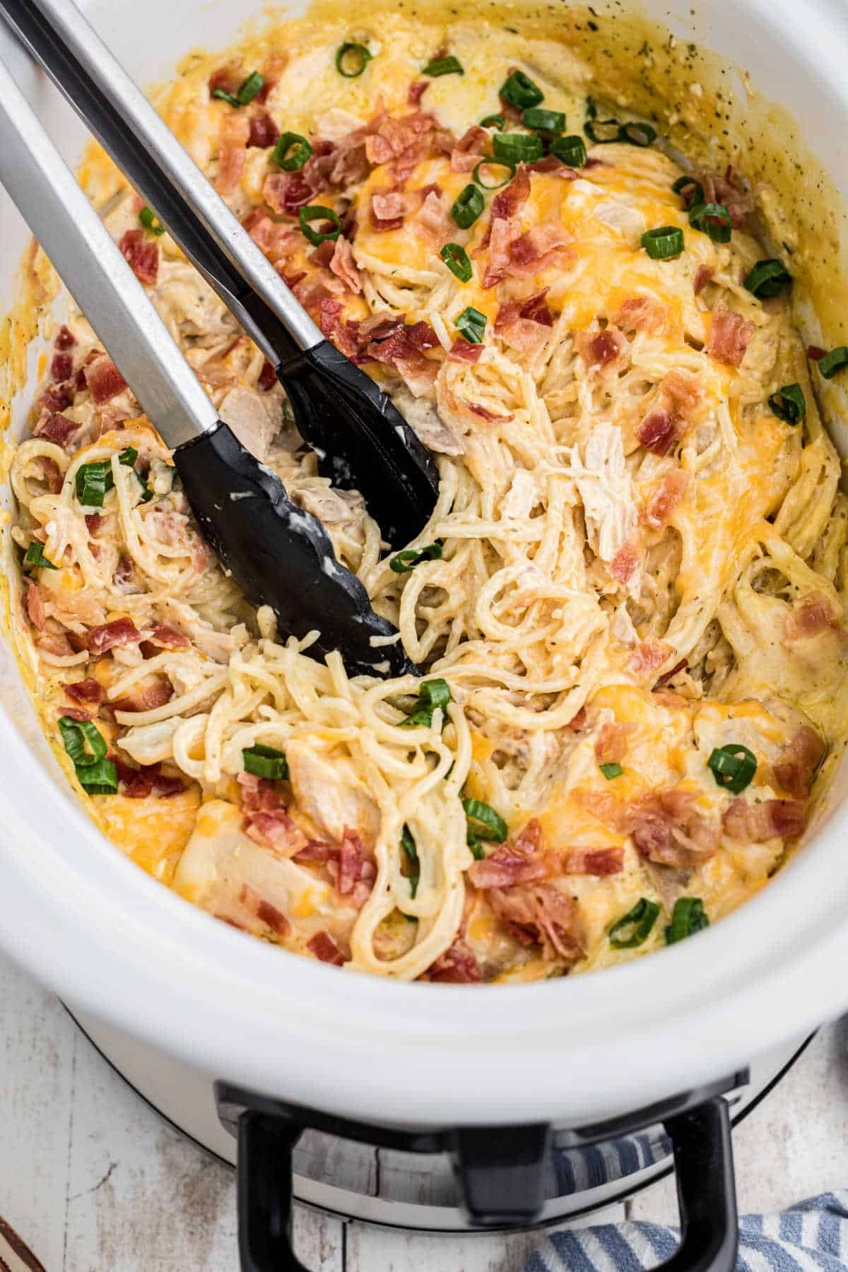 Overhead shot of a crock pot ranch chicken spaghetti recipe with tongs digging in.