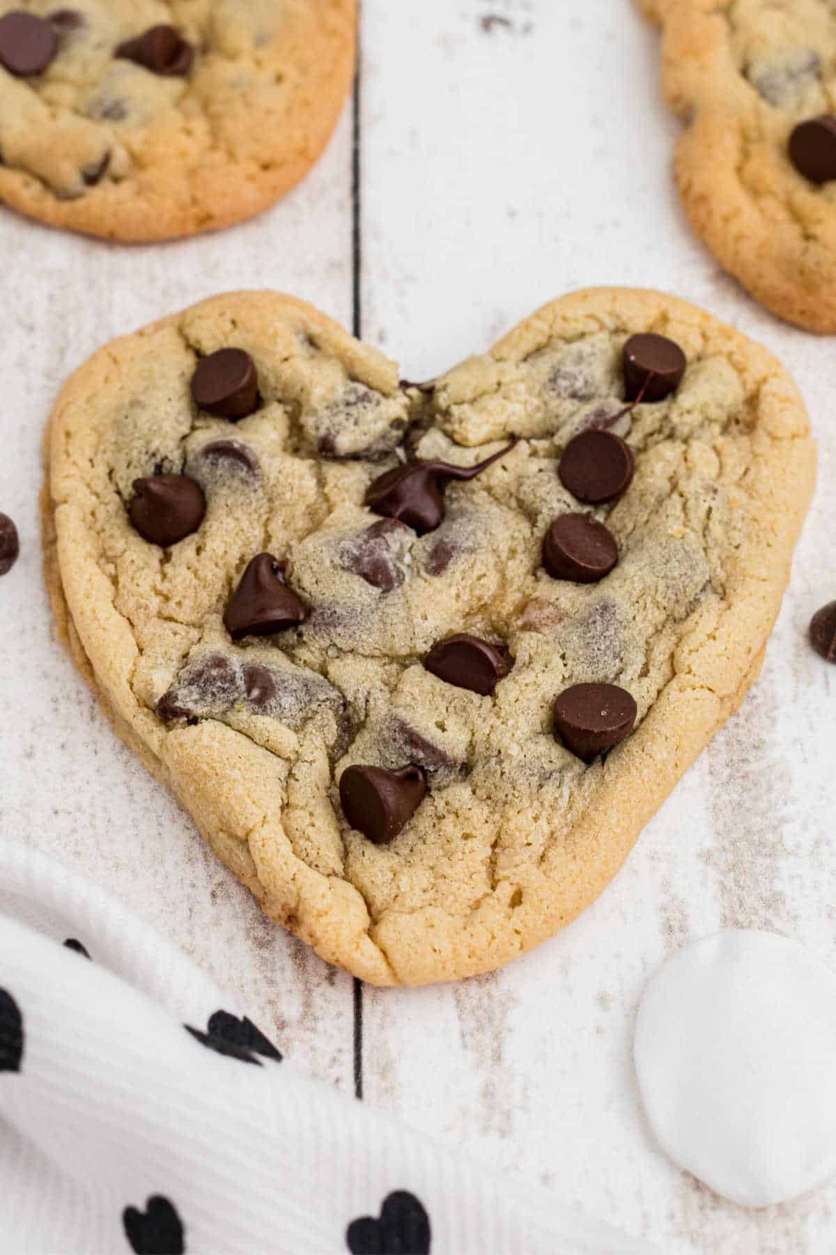 Side view of a heart shaped chocolate chip cookie, with more in the background.