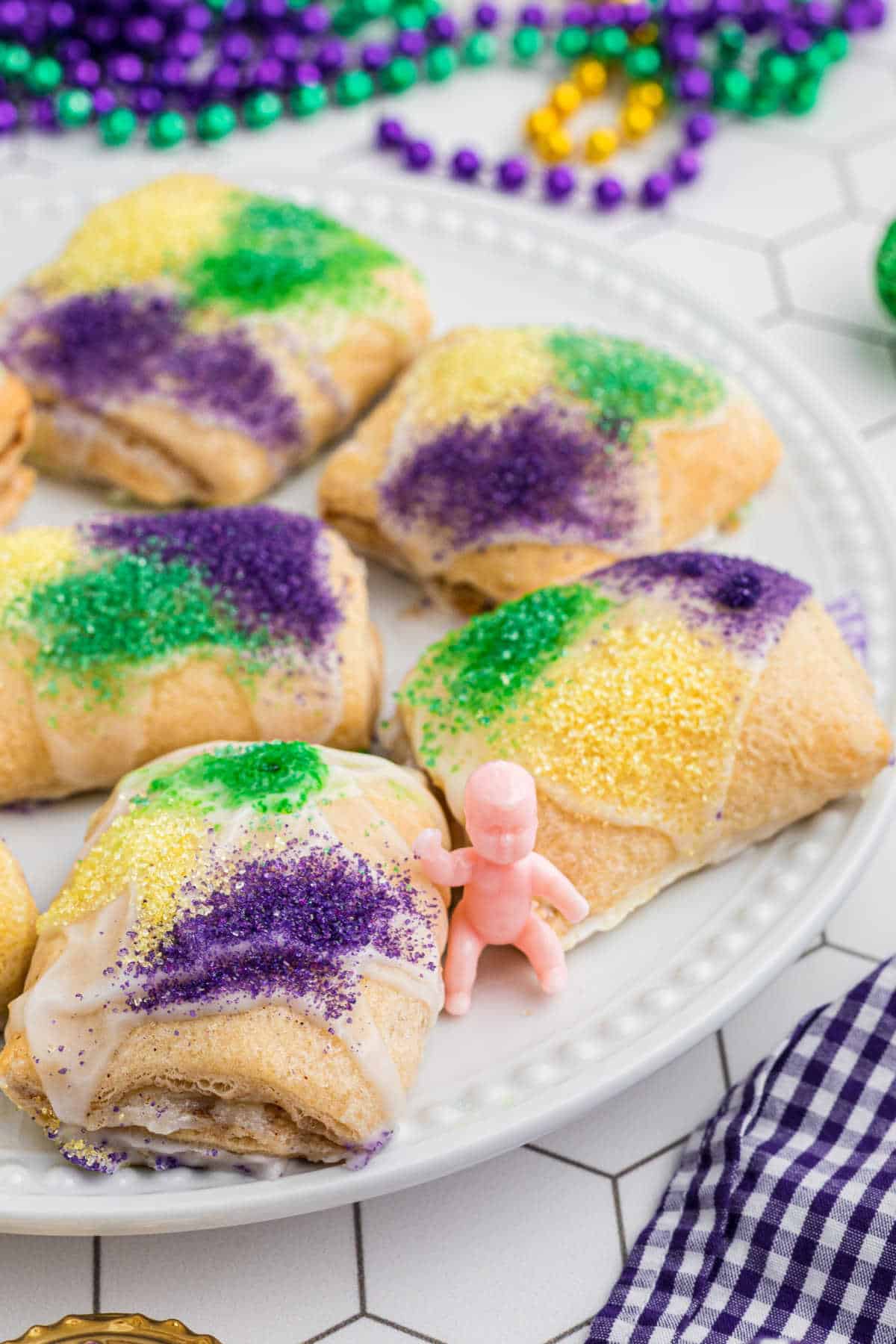 Long image of a plate full of little king cake bites with a king cake baby.
