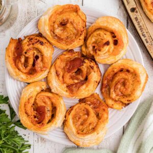 A close up overhead shot of a plate full of puff pastry pizza pinwheels, cropped square.