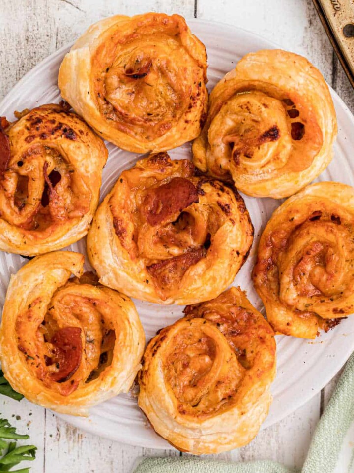 A close up overhead shot of a plate full of puff pastry pizza pinwheels, cropped square.