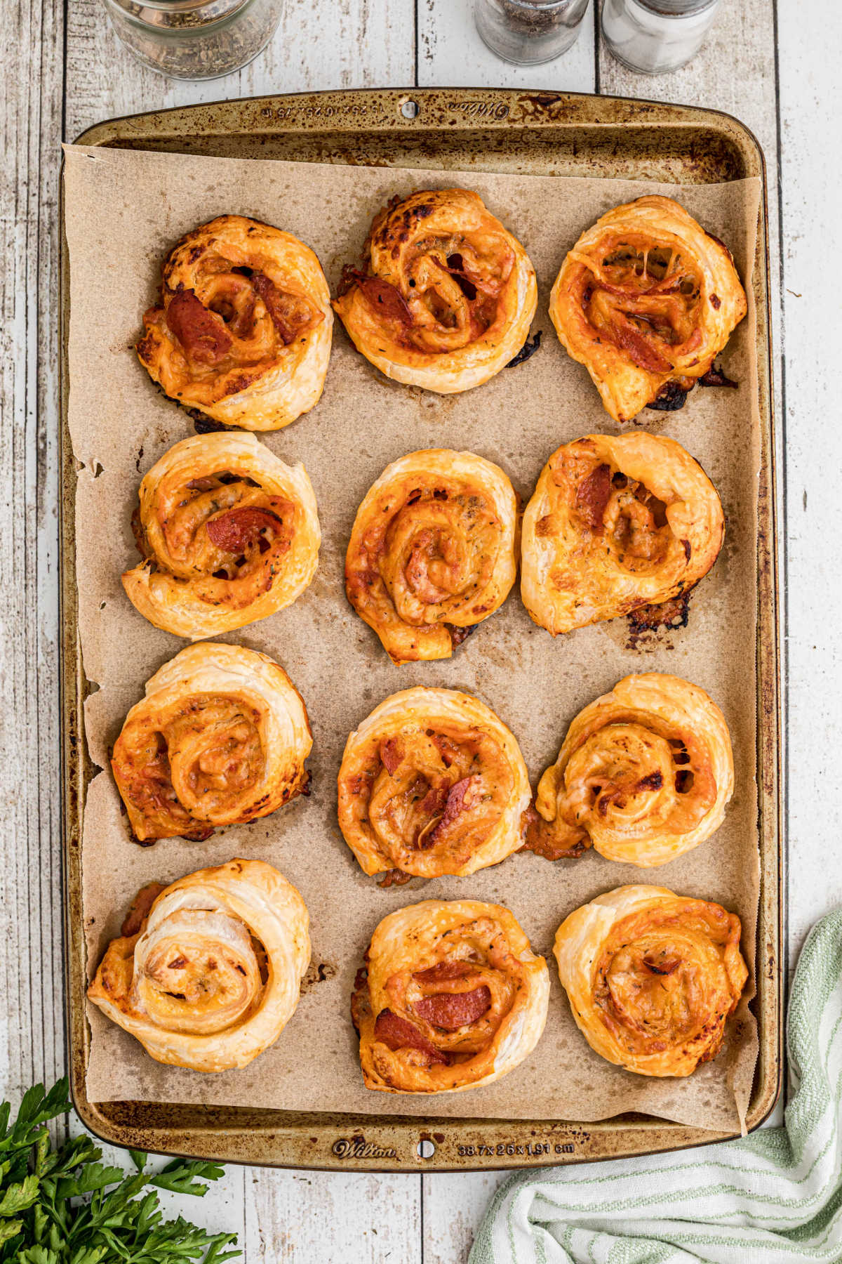 A baking sheet with parchment paper full of puff pastry pizza pinwheels.