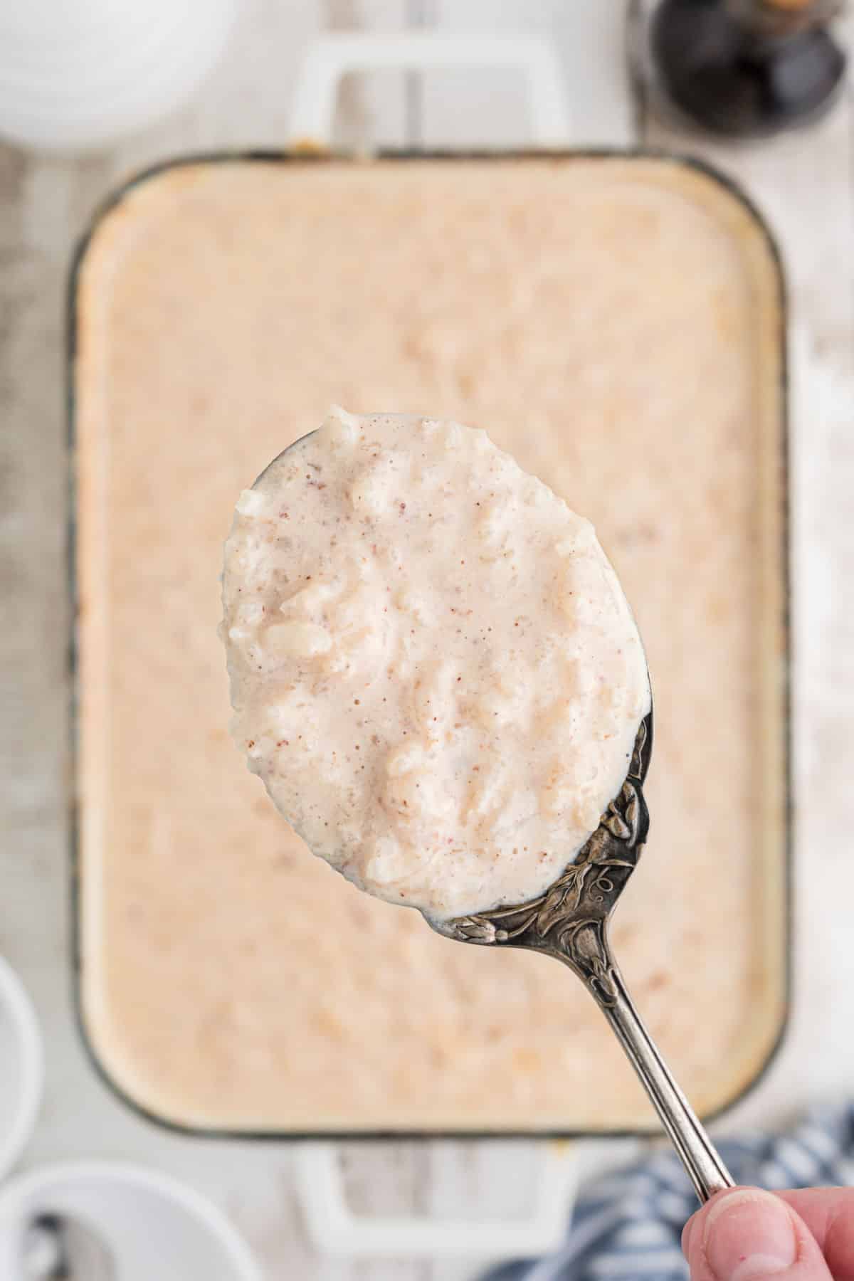 A spoon being lifted out of a pan full of rice pudding with evaporated milk.