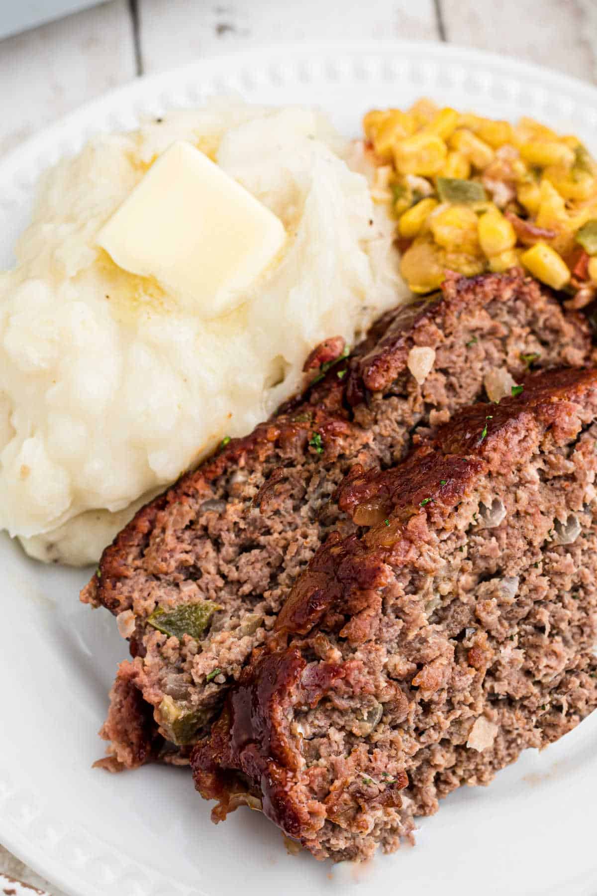 A close up image of a plate of meatloaf with mashed potatoes and corn.