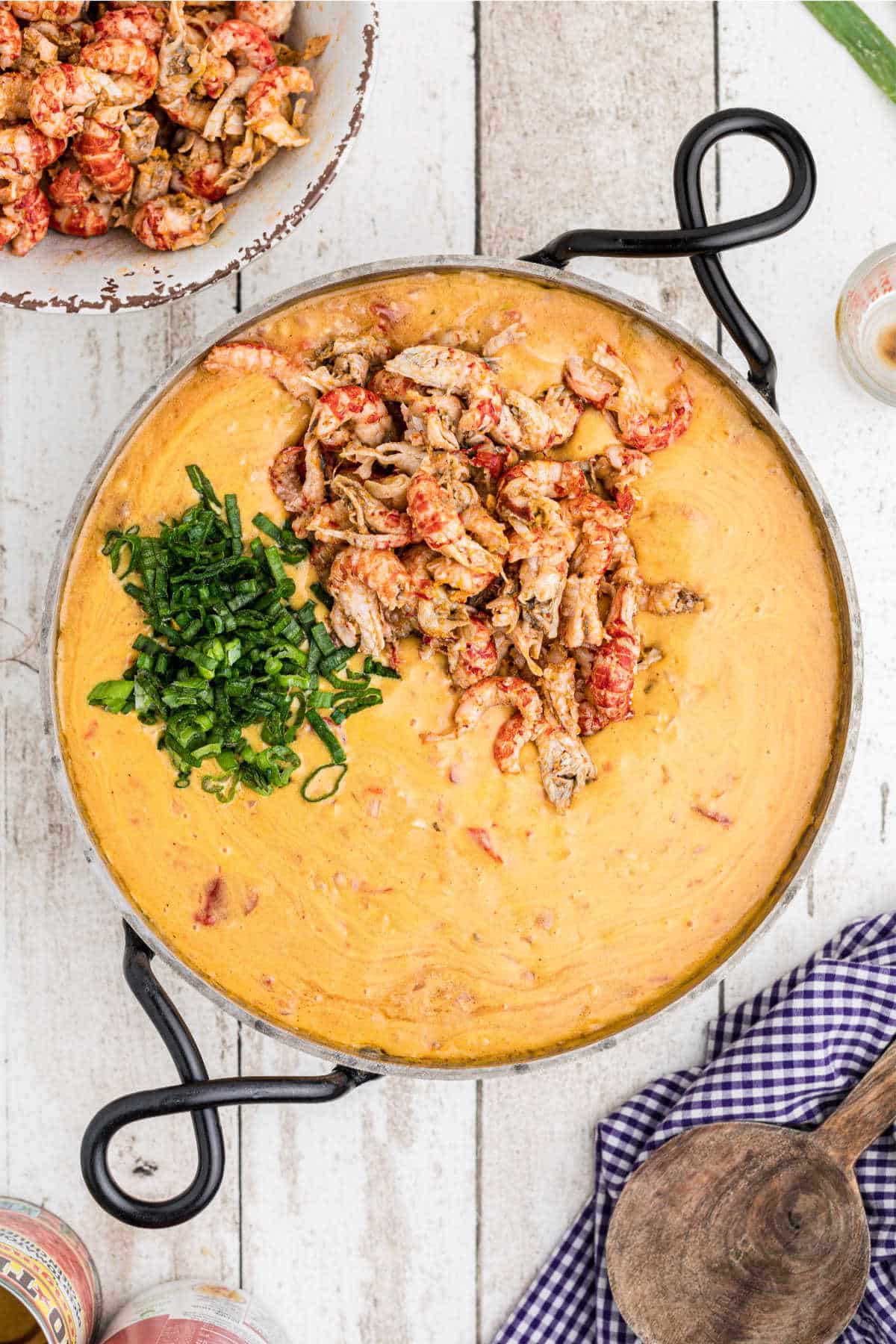Crawfish tails and chopped green onions in a skillet with a cheesy sauce.