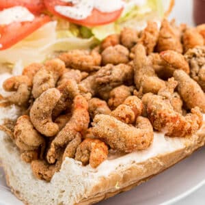 Close up of fried crawfish on a bread dressed with lettuce tomatoes and mayonnaise.
