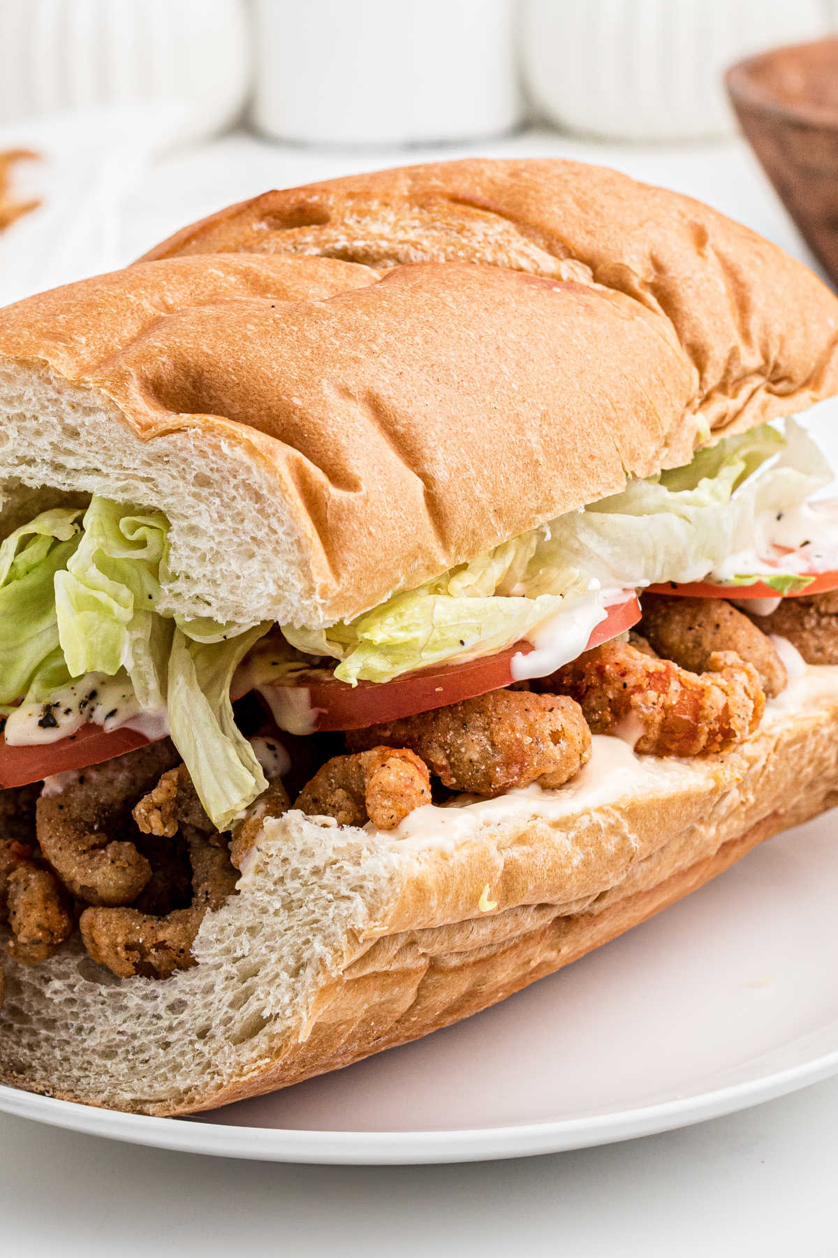 Close up of a bread sub filled with fried crawfish , dressed with lettuce, tomato and mayonnaise.