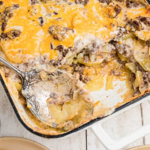 A hamburger potato casserole with a spoon with some missing, it's cropped square.