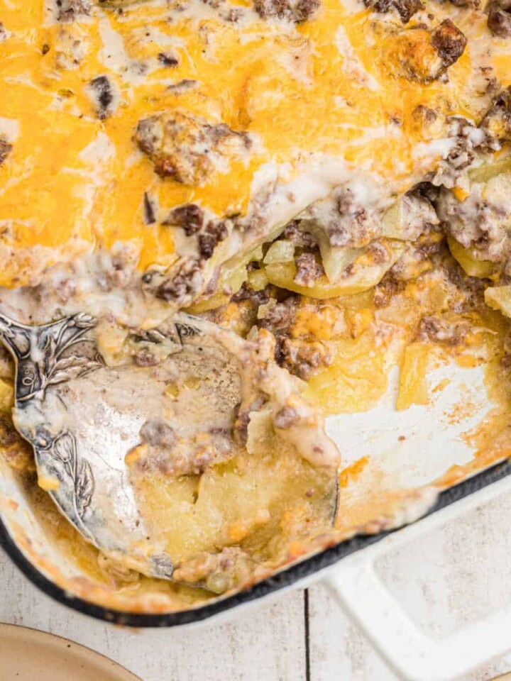 A hamburger potato casserole with a spoon with some missing, it's cropped square.