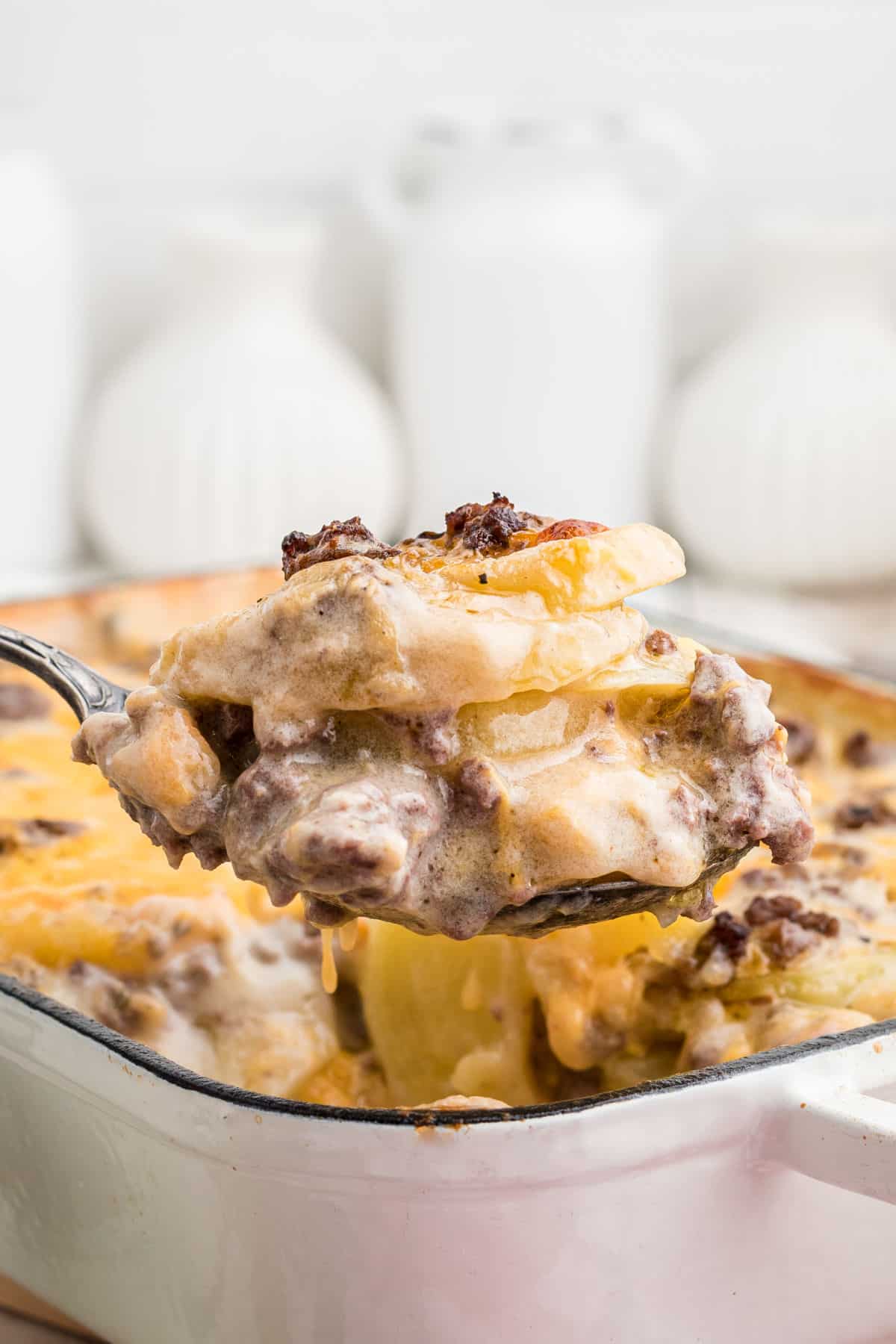 Close up of a spoon coming out of a casserole dish - it's a hamburger potato casserole.