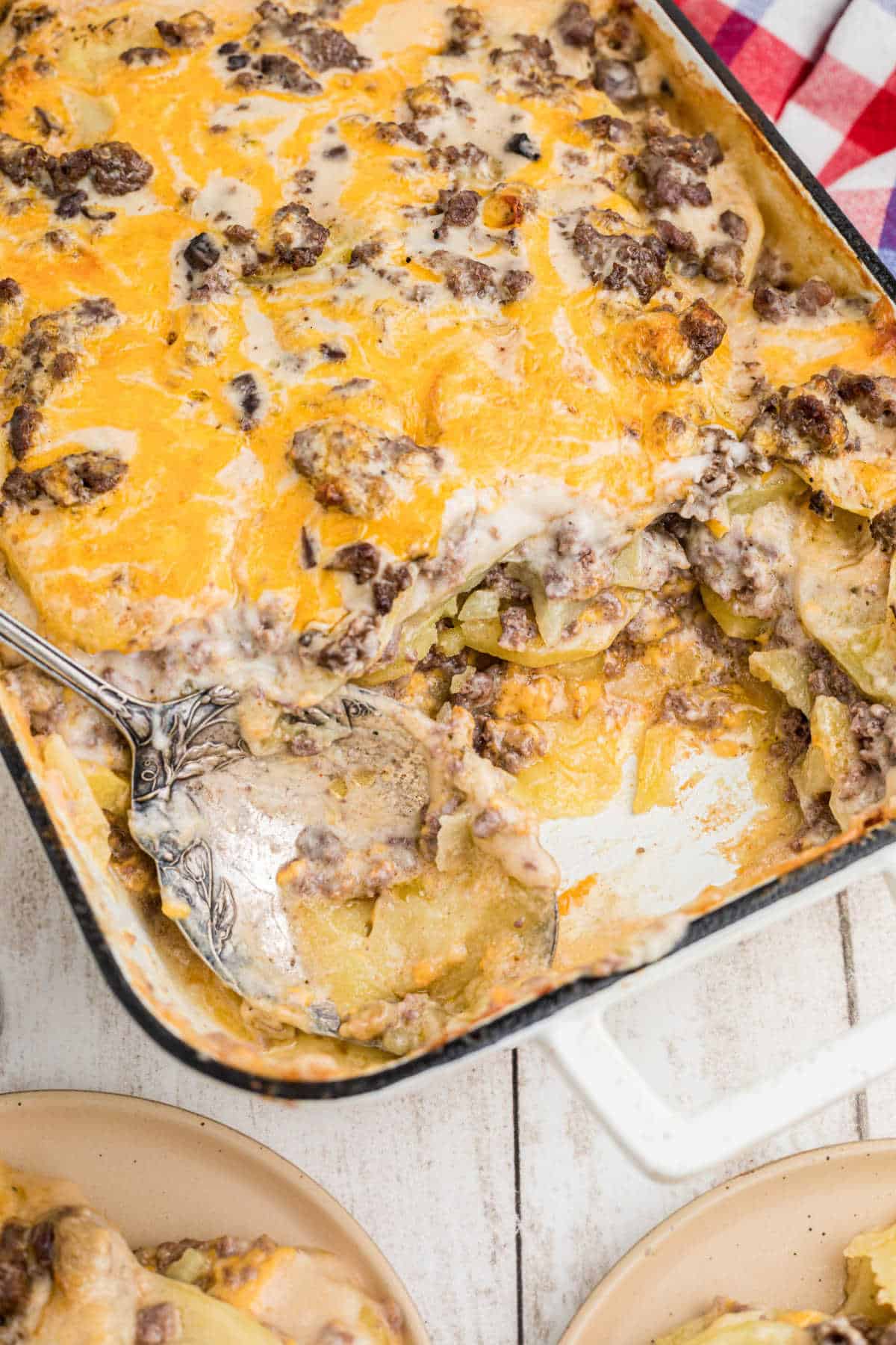 Overhead portrait shot of a hamburger potato casserole with a spoon resting in the spot where there's some of the casserole missing.