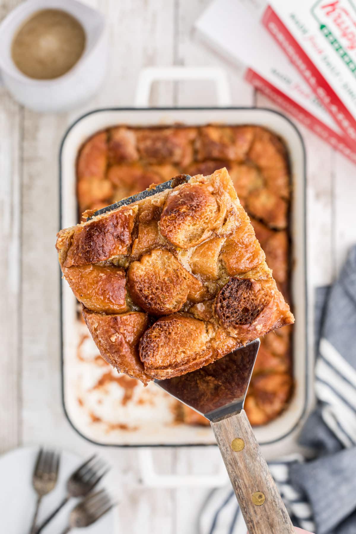 A slice being lifted out of a dish full of bread pudding made out of krispy kreme doughnuts.