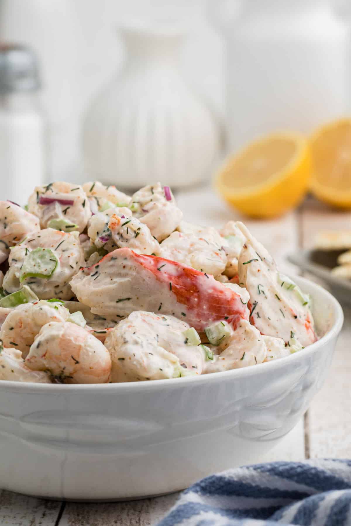 A close up of a dish heaped with southern seafood salad with some lemons in the background.