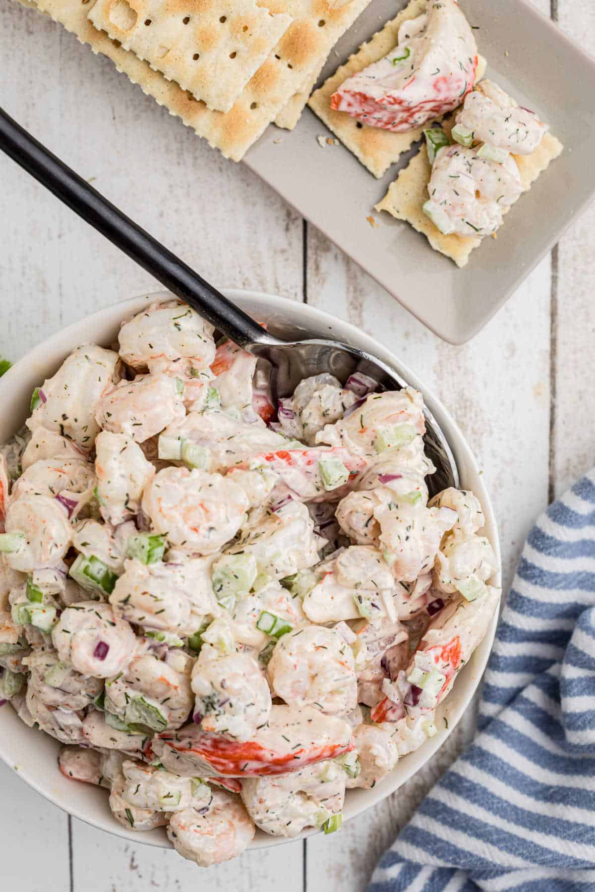 A bowl of seafood salad with a spoon and some crackers.