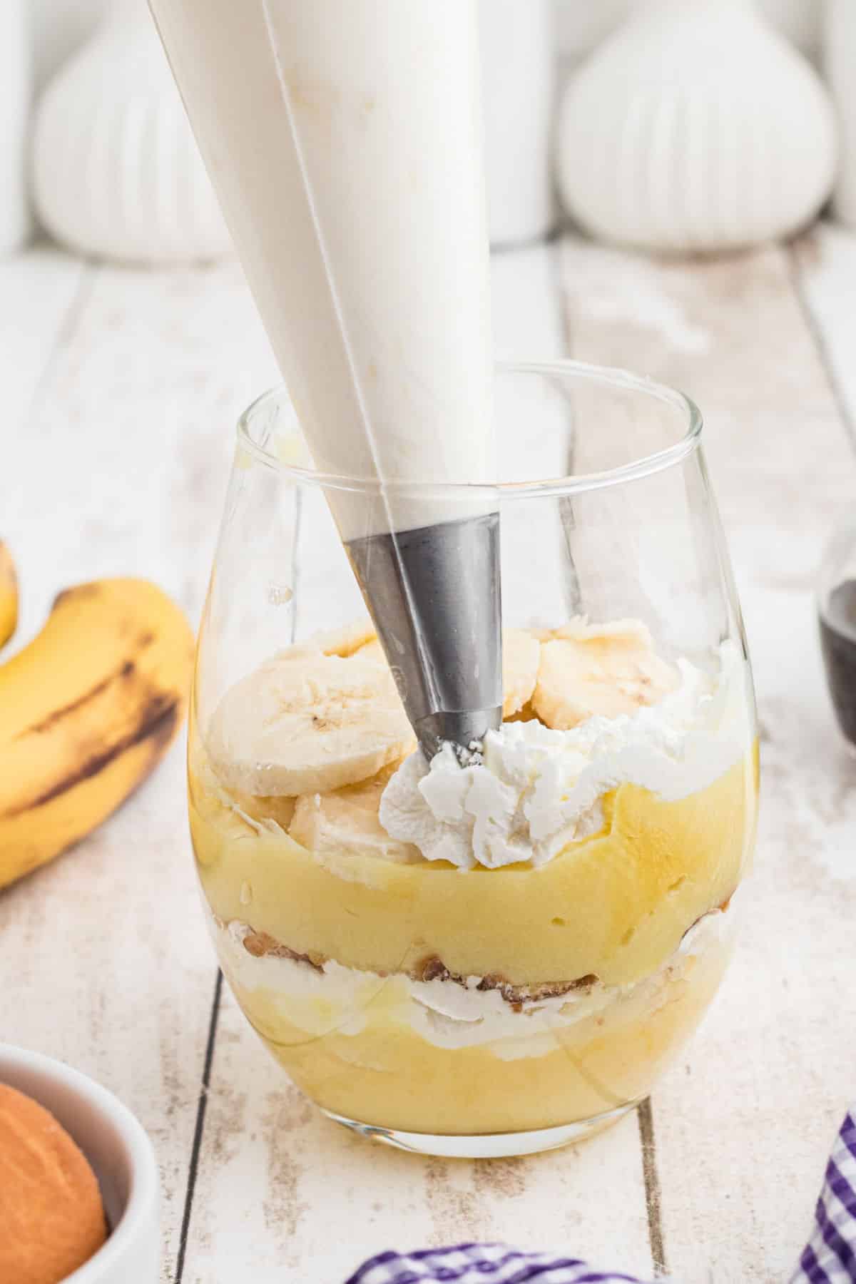 A glass being filled in layers making banana pudding cups.